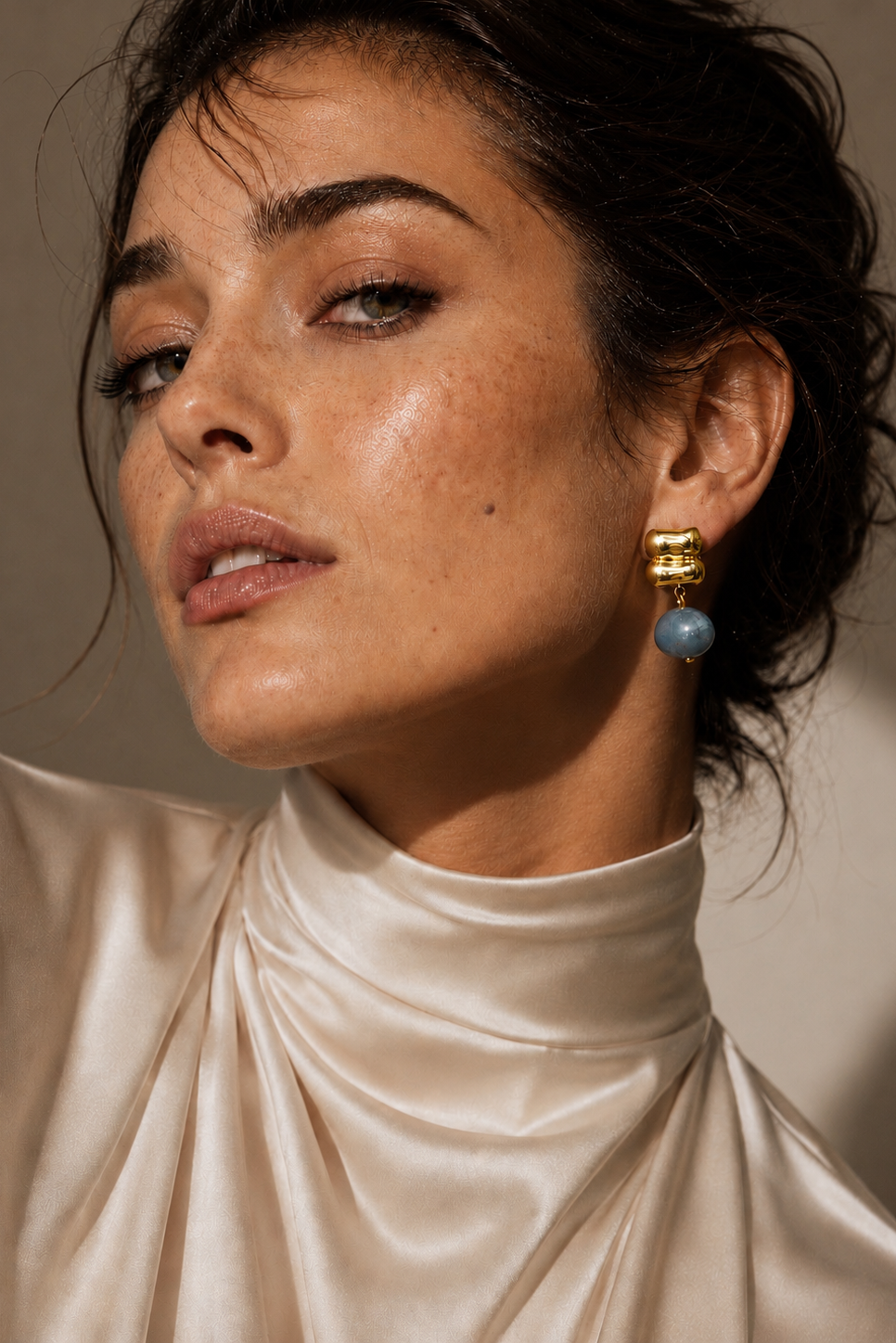 Woman wearing gold and blue earrings against a neutral background