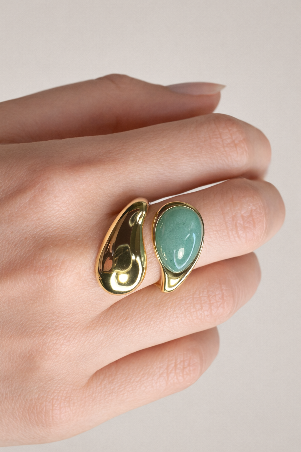 Gold ring with a turquoise stone on a hand against a neutral background