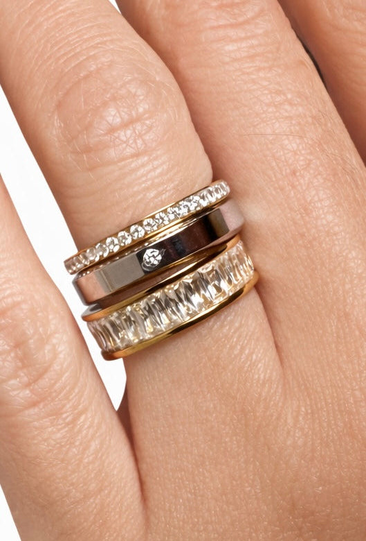 Close-up of a hand wearing a set of three gold rings with different designs on a neutral background