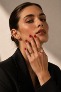 Woman wearing a black outfit with a gold ring on her finger against a neutral background