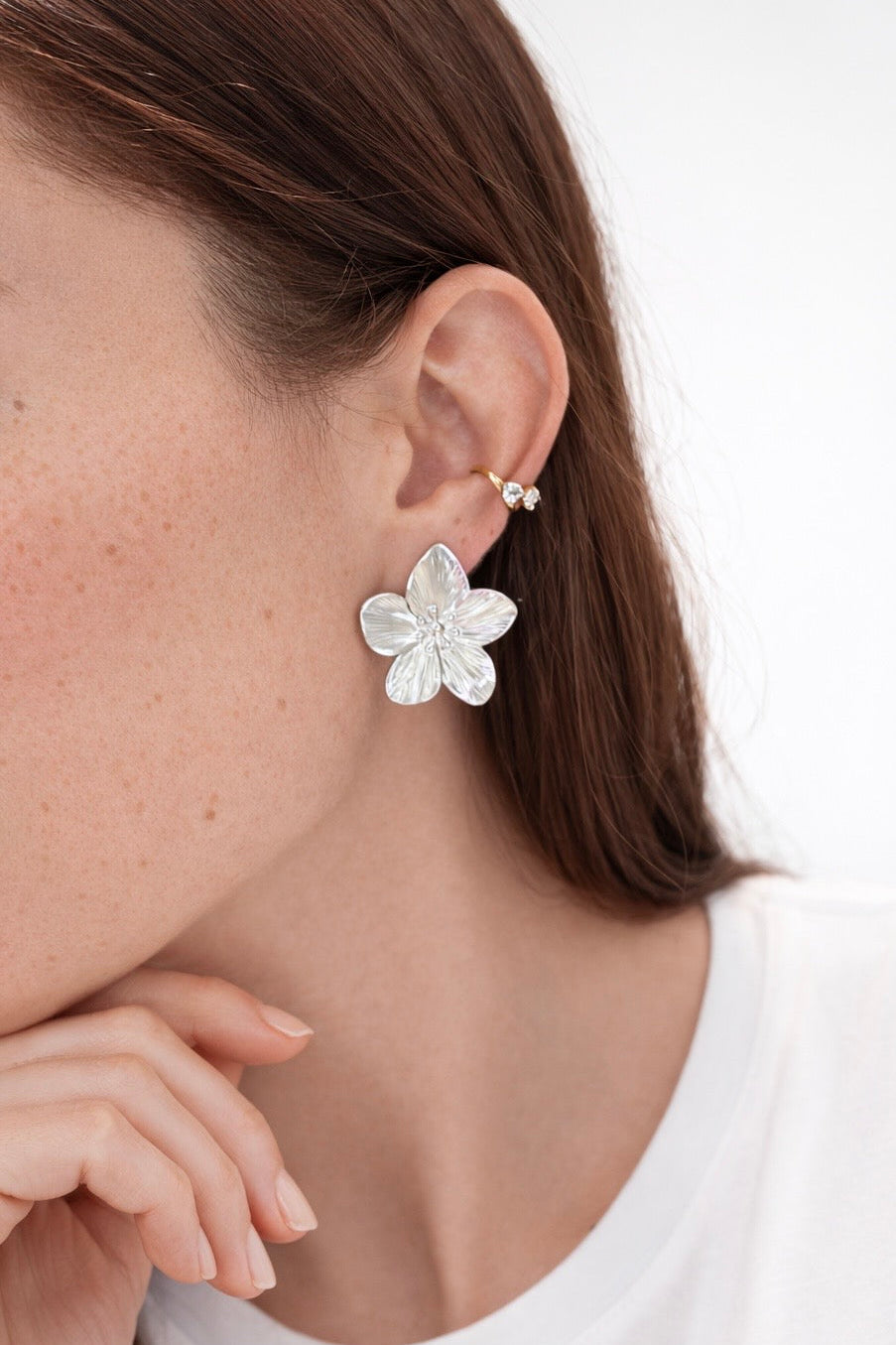 Flower-shaped earring worn by a person on a white background