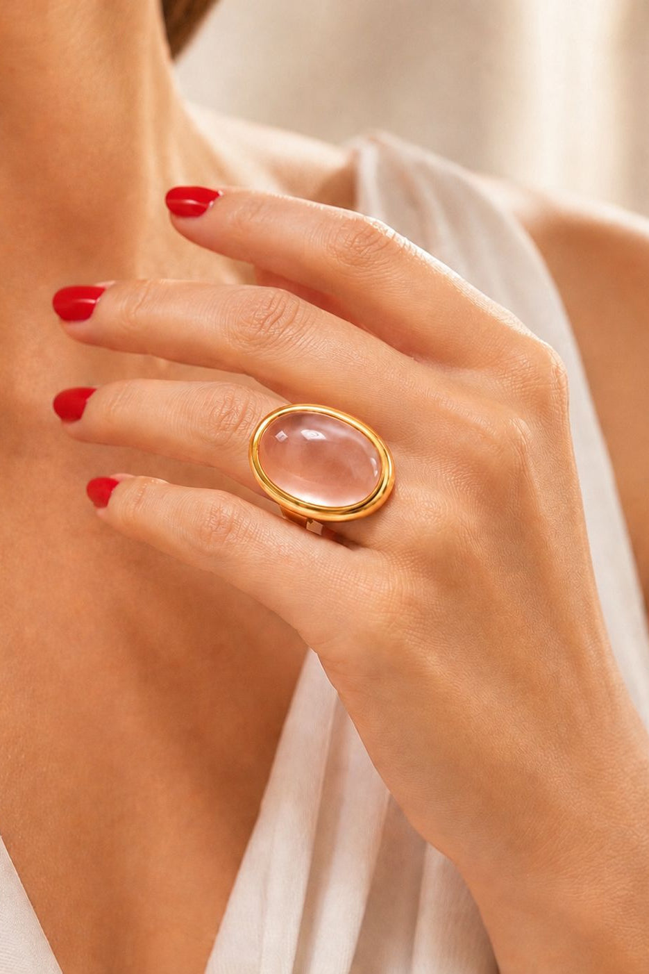 Hand wearing a gold ring with a transparent glass, against a neutral background