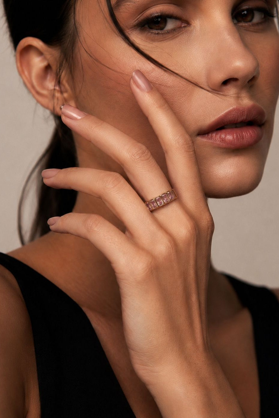 Close-up of a woman's hand with a ring, wearing a black top against a neutral background