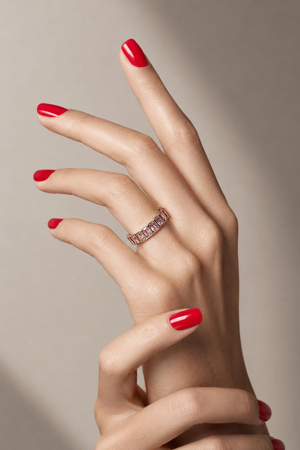 Hand with red nail polish wearing a ring on a neutral background