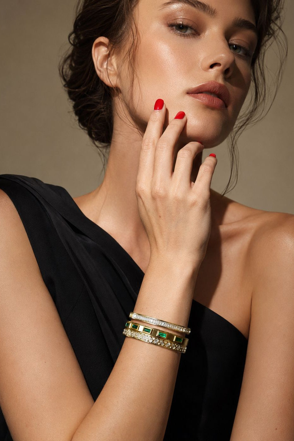 Woman wearing gold and green bracelets on a neutral background