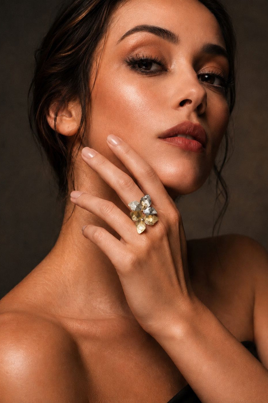 Woman wearing a ring with multiple gemstones against a dark background