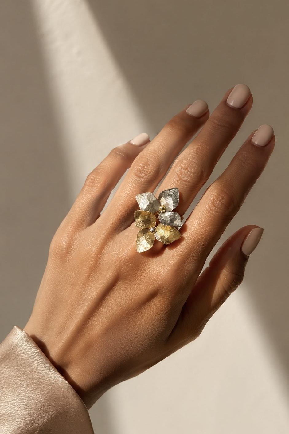 Hand wearing a ring with multiple gemstones against a neutral background