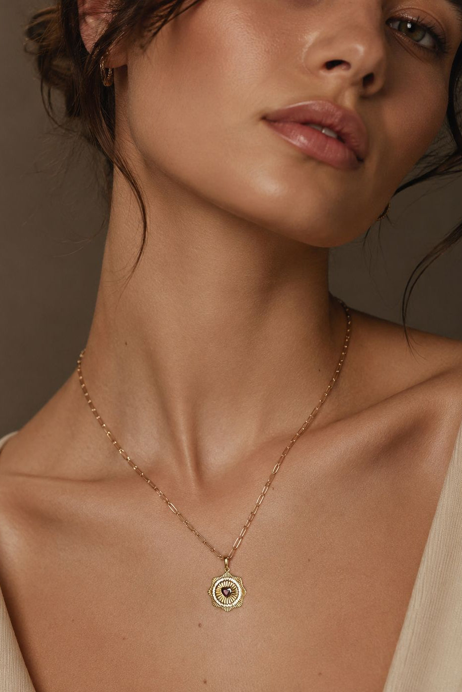 Close-up of a woman wearing a gold necklace with a pendant against a neutral background