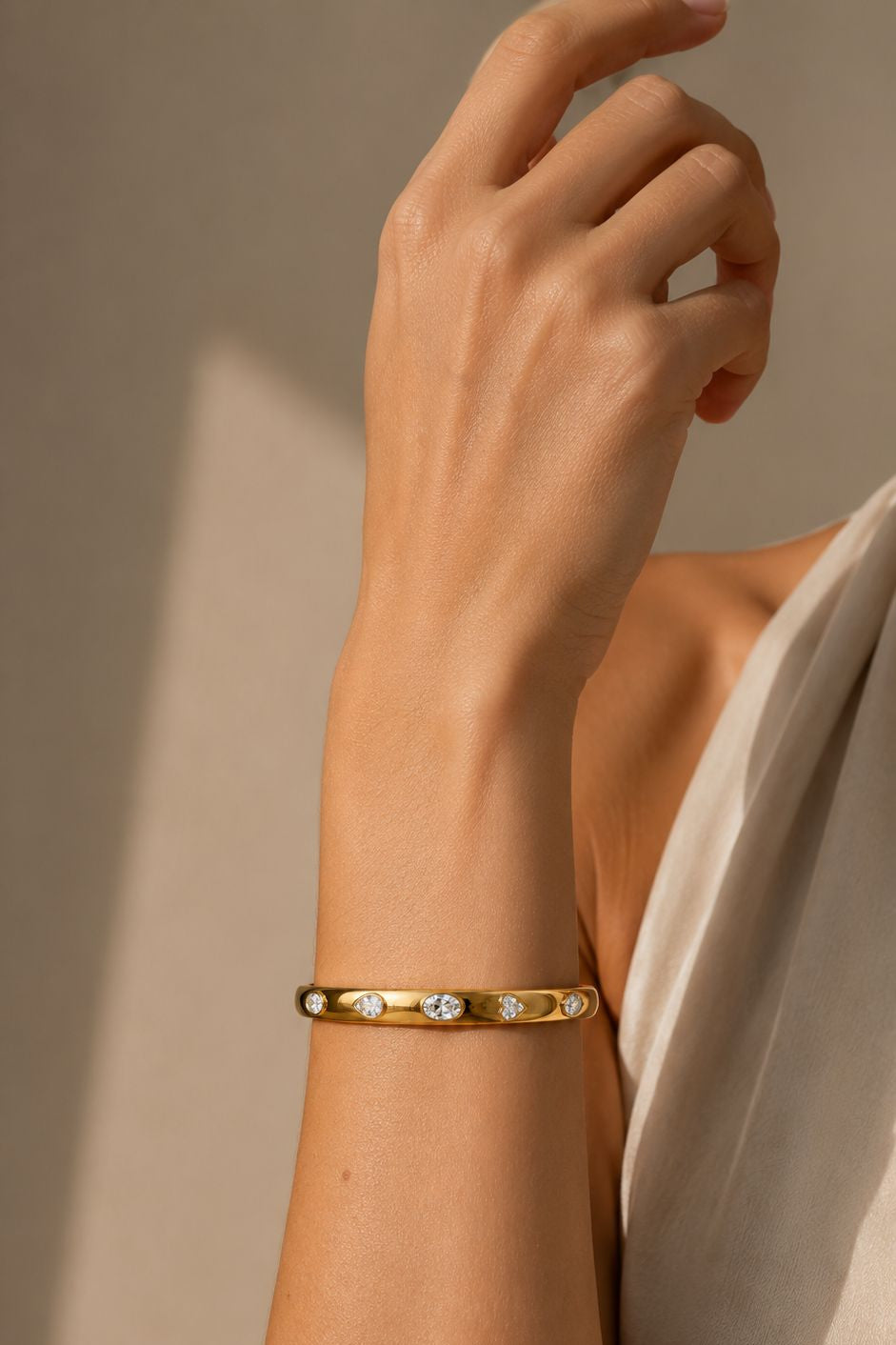 Gold bracelet with small stones on a wrist against a neutral background