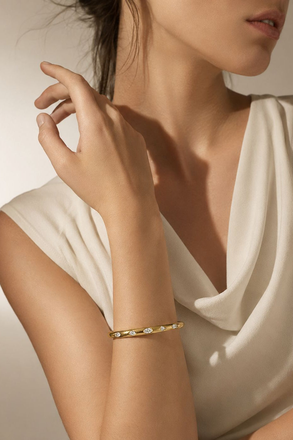 Woman wearing a gold bracelet on a neutral background