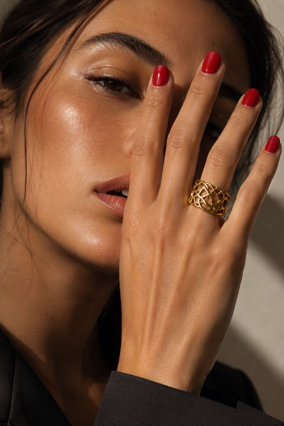 Woman wearing a gold ring with red nail polish on a neutral background