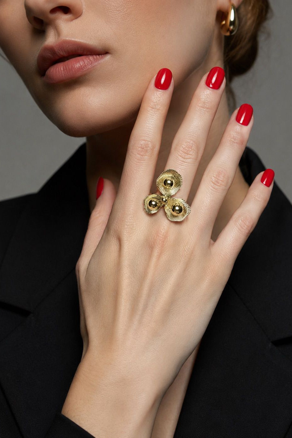 Close-up of a woman's hand wearing a gold ring with red nail polish on a gray background