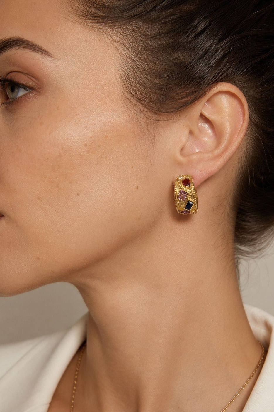 Close-up of a person wearing gold hoop earrings with gemstones.