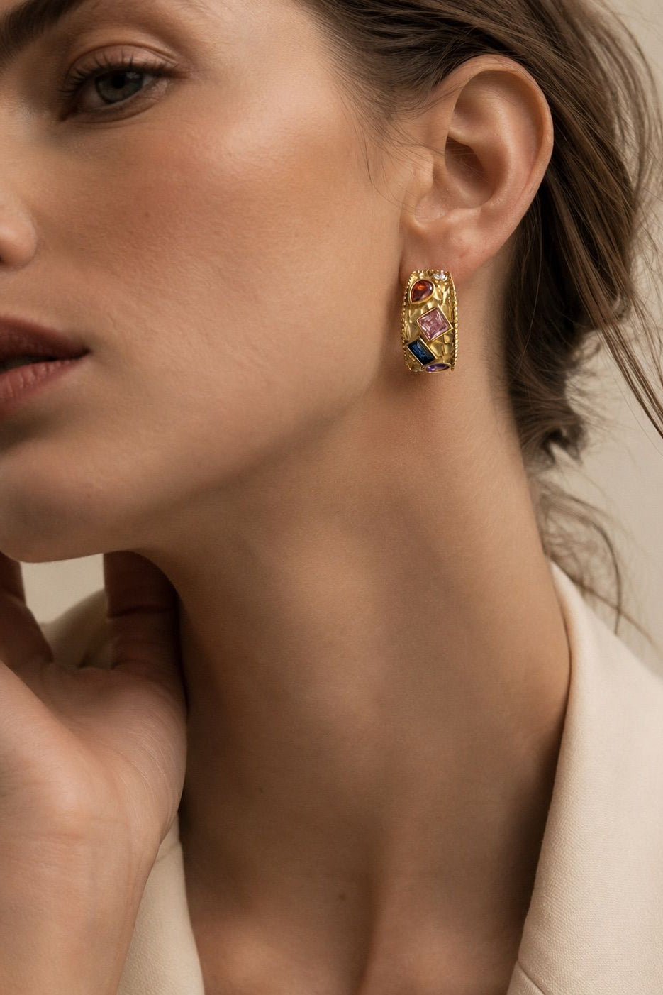 Close-up of a woman wearing colorful hoop earrings with a neutral background