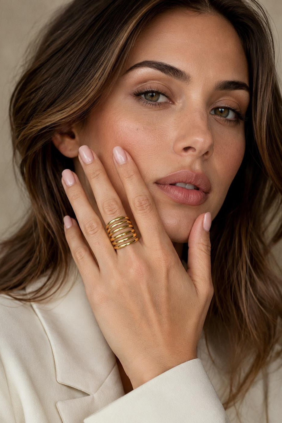 Woman wearing gold rings on a neutral background