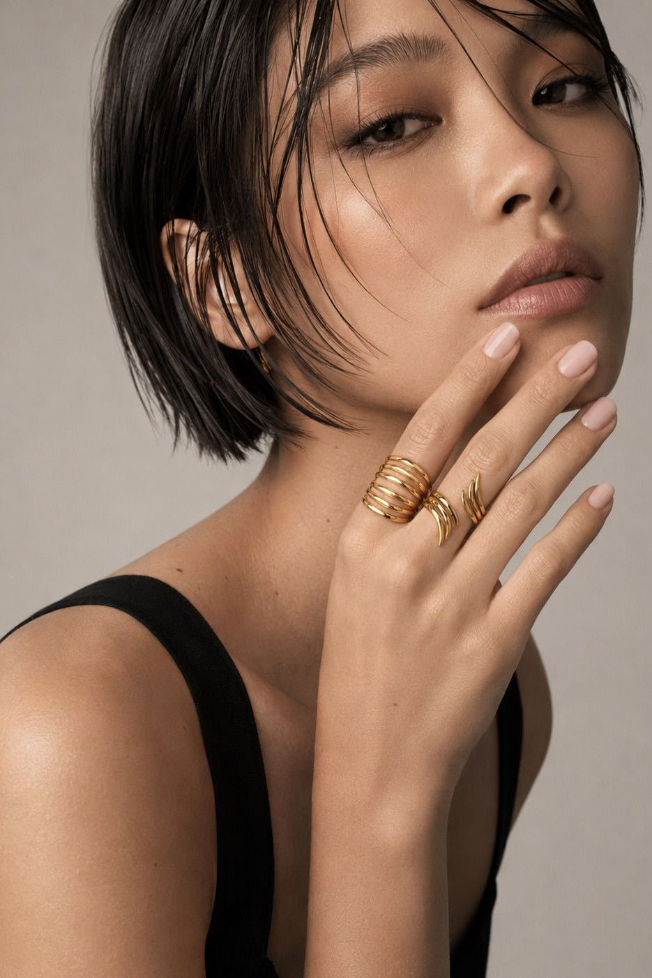 Woman wearing gold rings on a neutral background