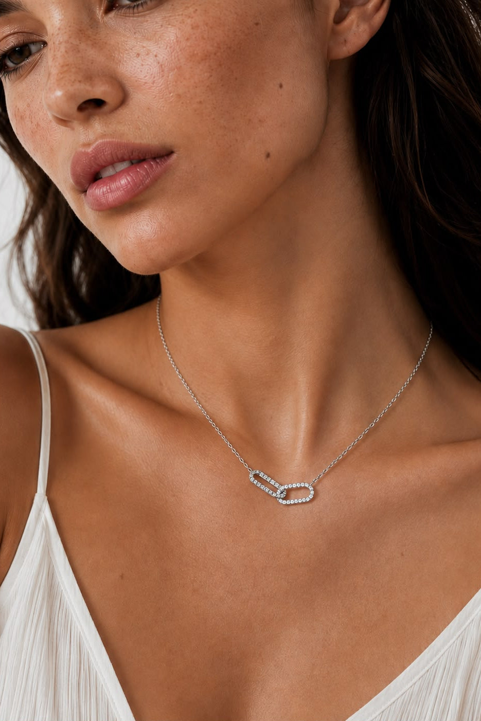 Close-up of a woman wearing a delicate silver necklace against a neutral background