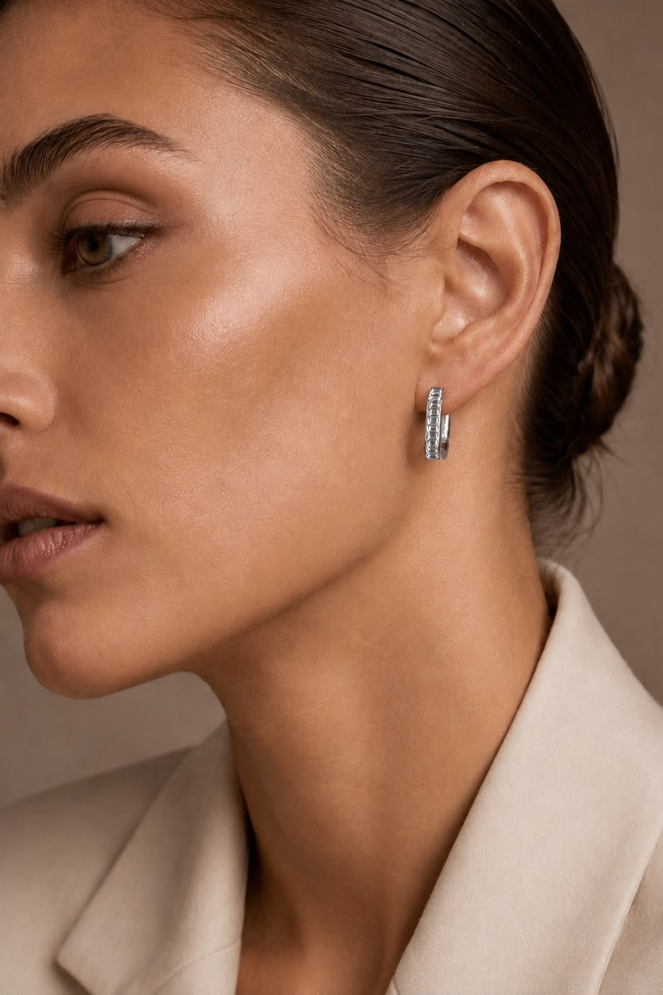 Close-up of a woman wearing a silver hoop earring against a neutral background