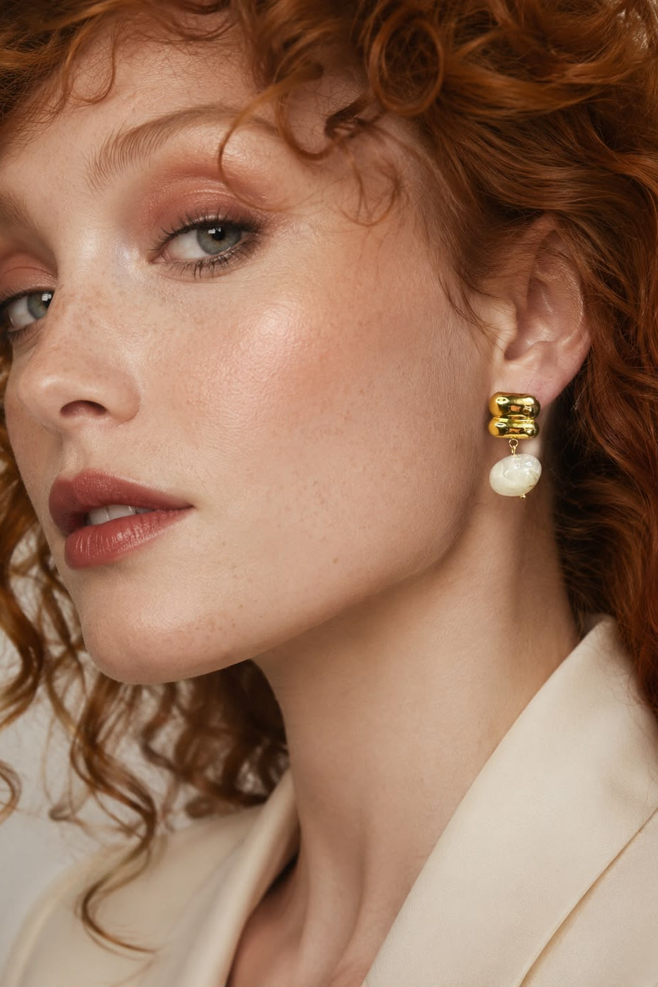 Close-up of a woman wearing gold earrings with pearl-like stones against a neutral background