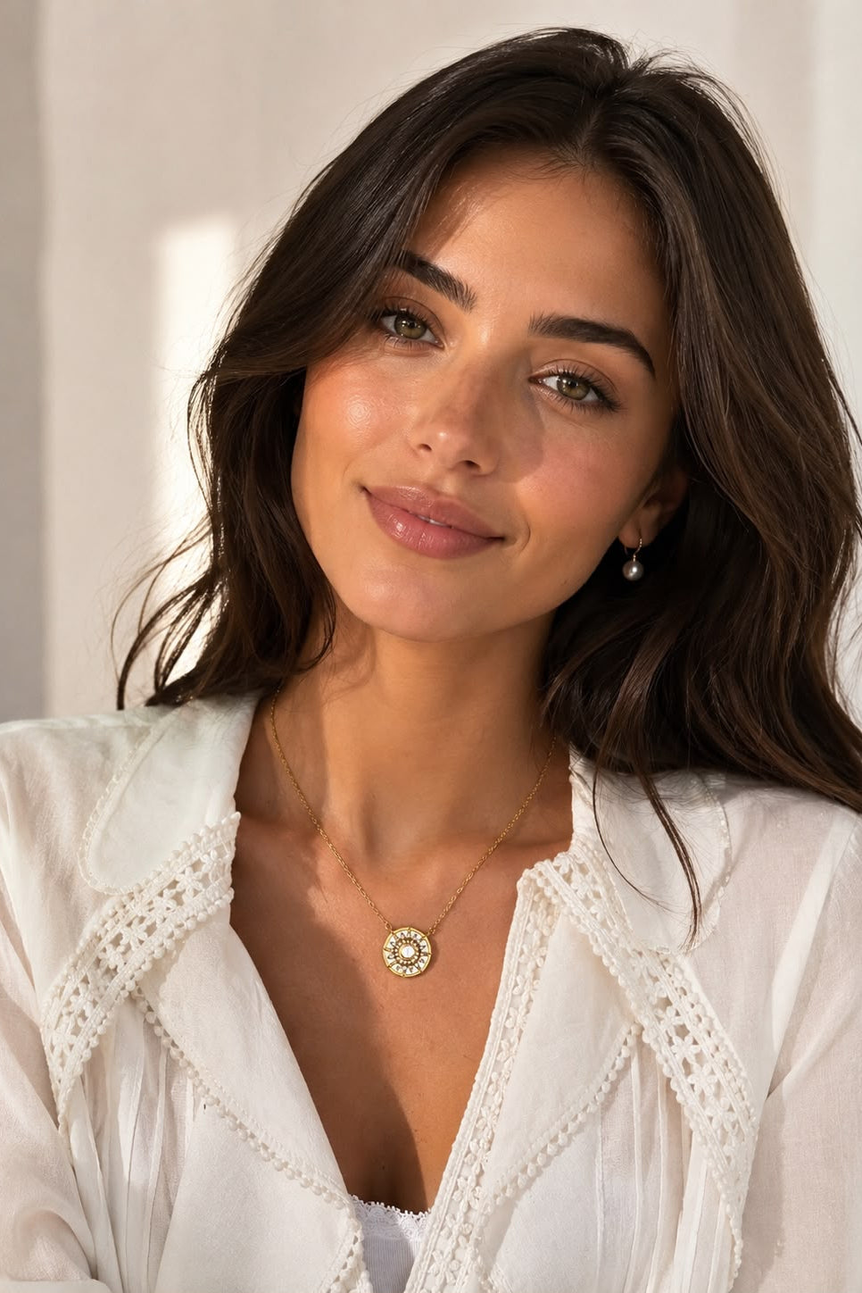 Woman wearing a white lace top with a gold necklace against a neutral background