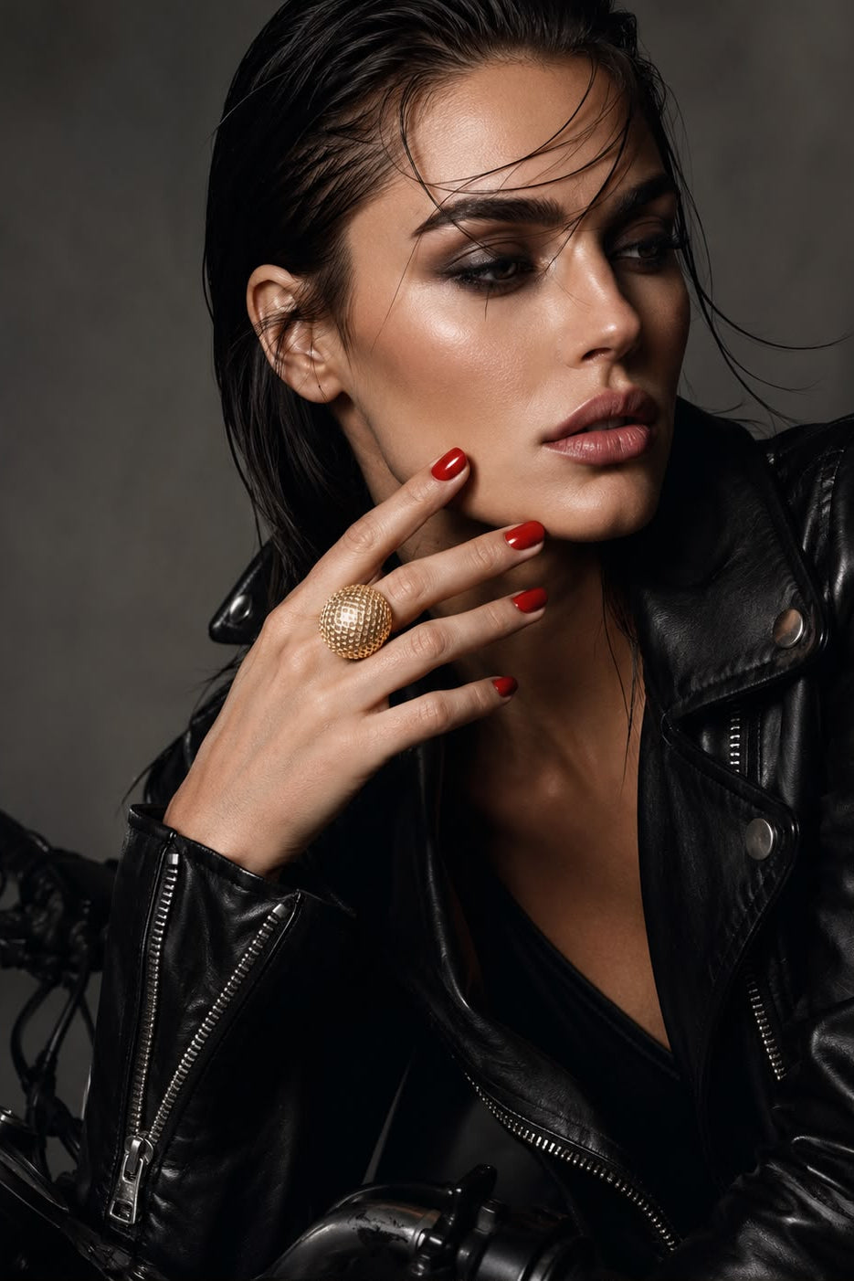 Woman wearing a black leather jacket with a gold ring on her finger against a dark background