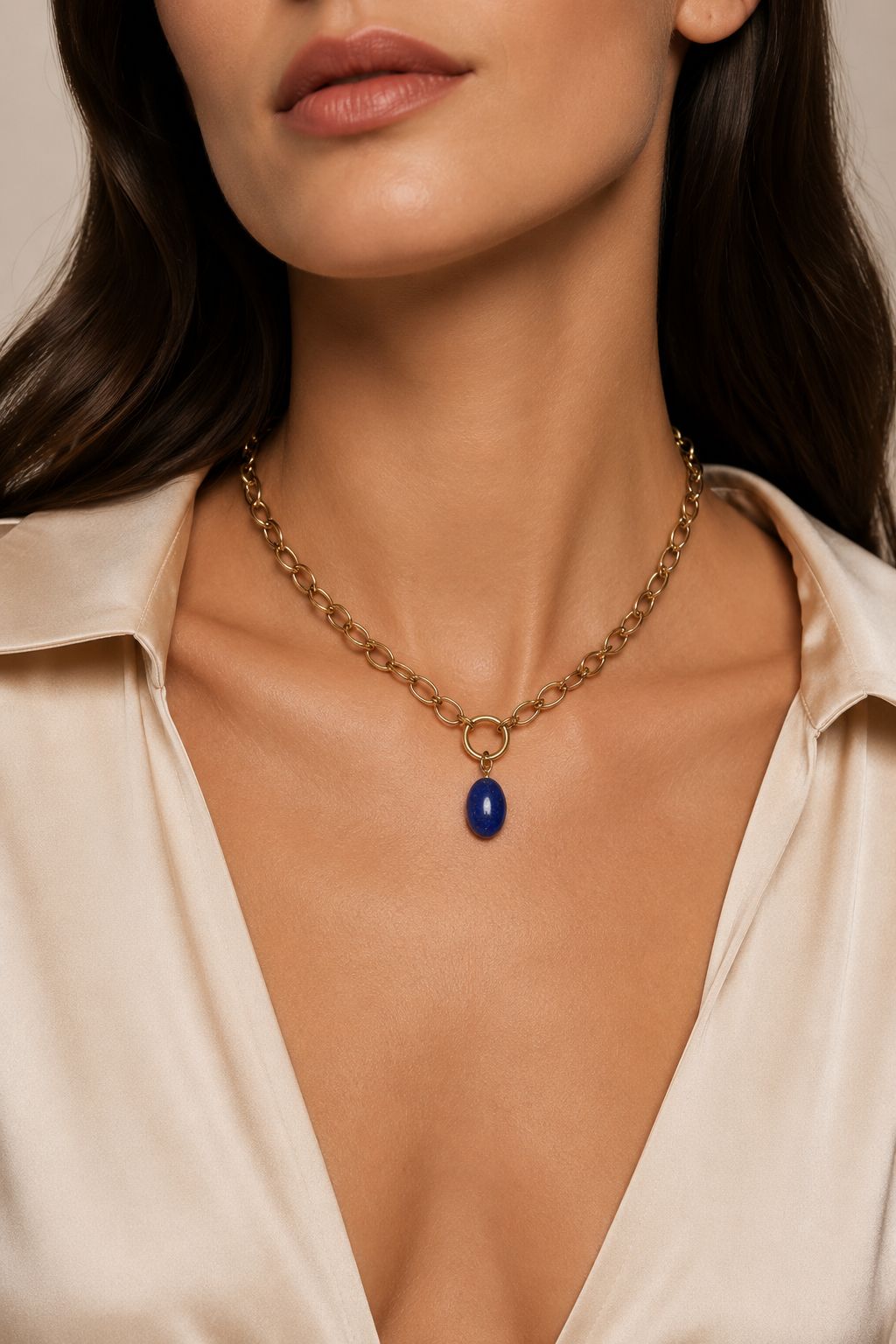 Necklace with a blue pendant worn by a person in a beige shirt.