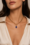 Necklace with a blue pendant worn by a person in a beige shirt.
