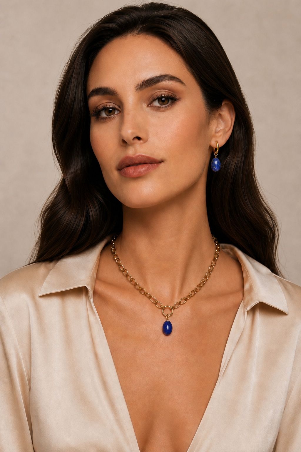Woman wearing a gold necklace with a blue pendant and matching earrings against a beige background