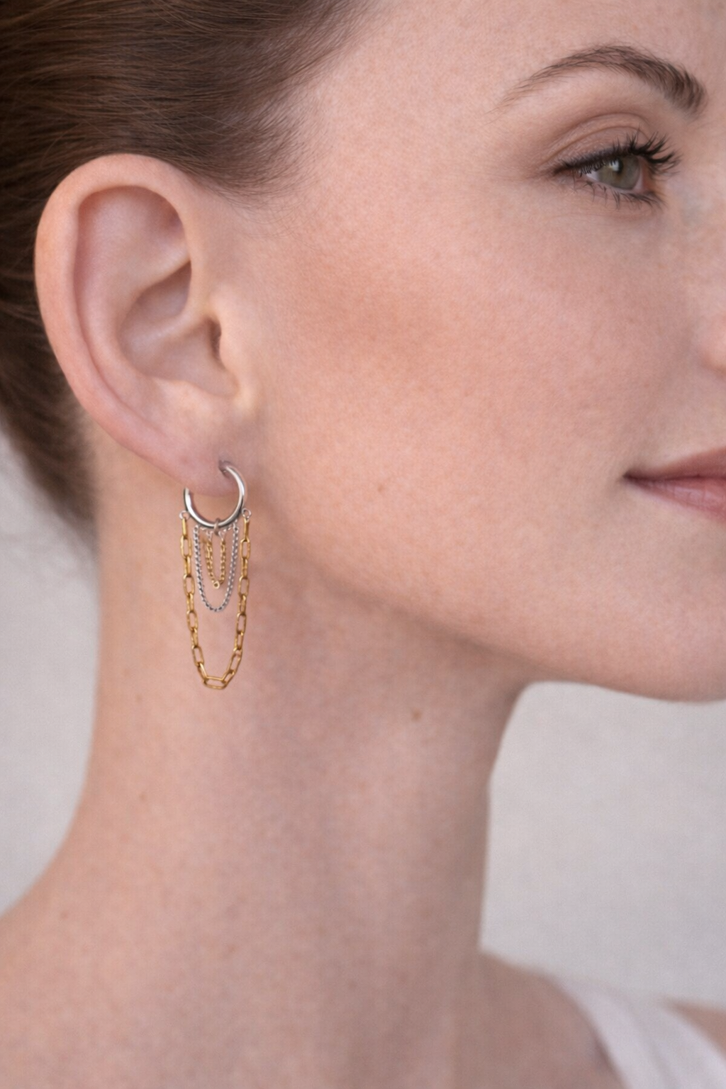 Close-up of a person wearing a gold hoop earring with a chain detail.