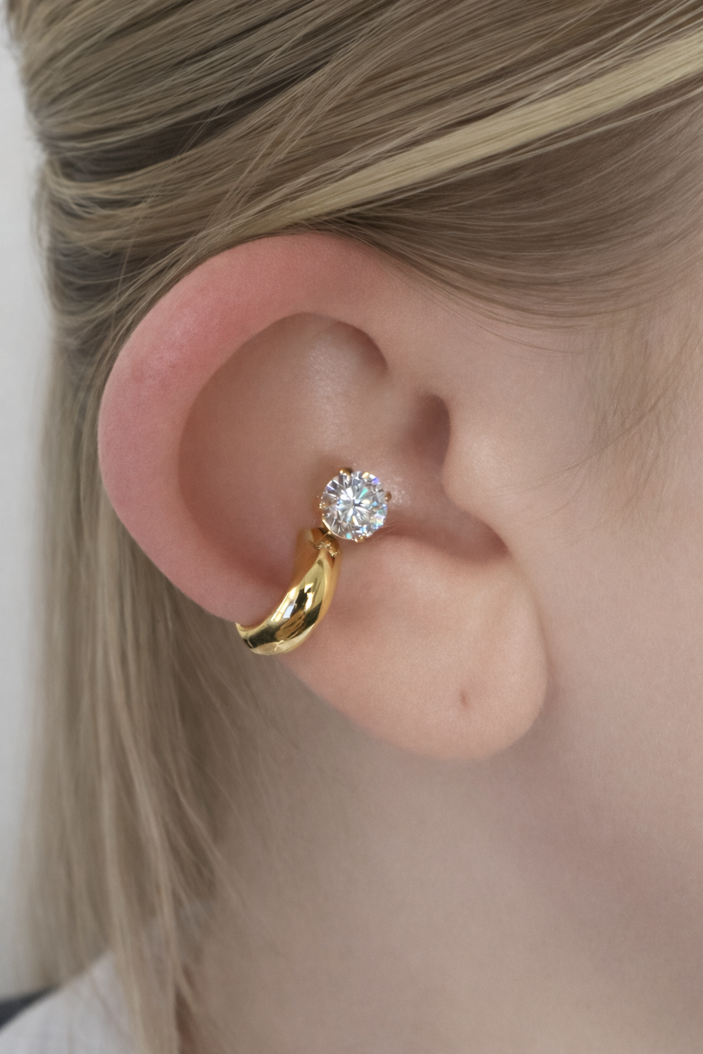 Close-up of a gold earring with a crystal on an ear against a neutral background