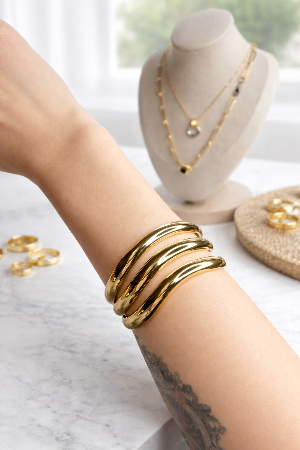 Gold-plated triple bracelet on a wrist with jewellery display in the background
